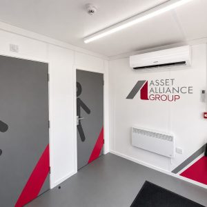 Entrance hallway with two doors showing large male/female restroom icons, gray panels with red diagonal accent, white walls.
