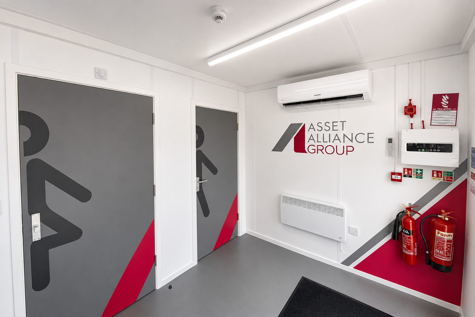 Entrance hallway with two doors showing large male/female restroom icons, gray panels with red diagonal accent, white walls.