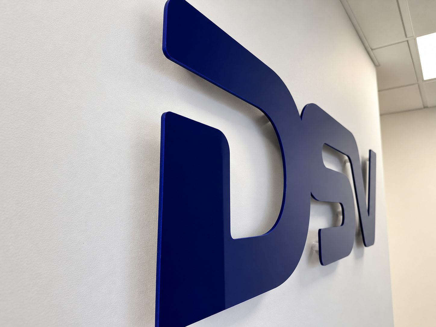 Blue 3D company logo letters mounted on a white wall in an office hallway (partially visible).