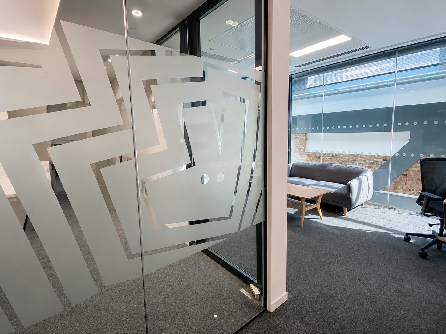 Frosted glass partition with overlapping square pattern, separating a conference room from a lounge.