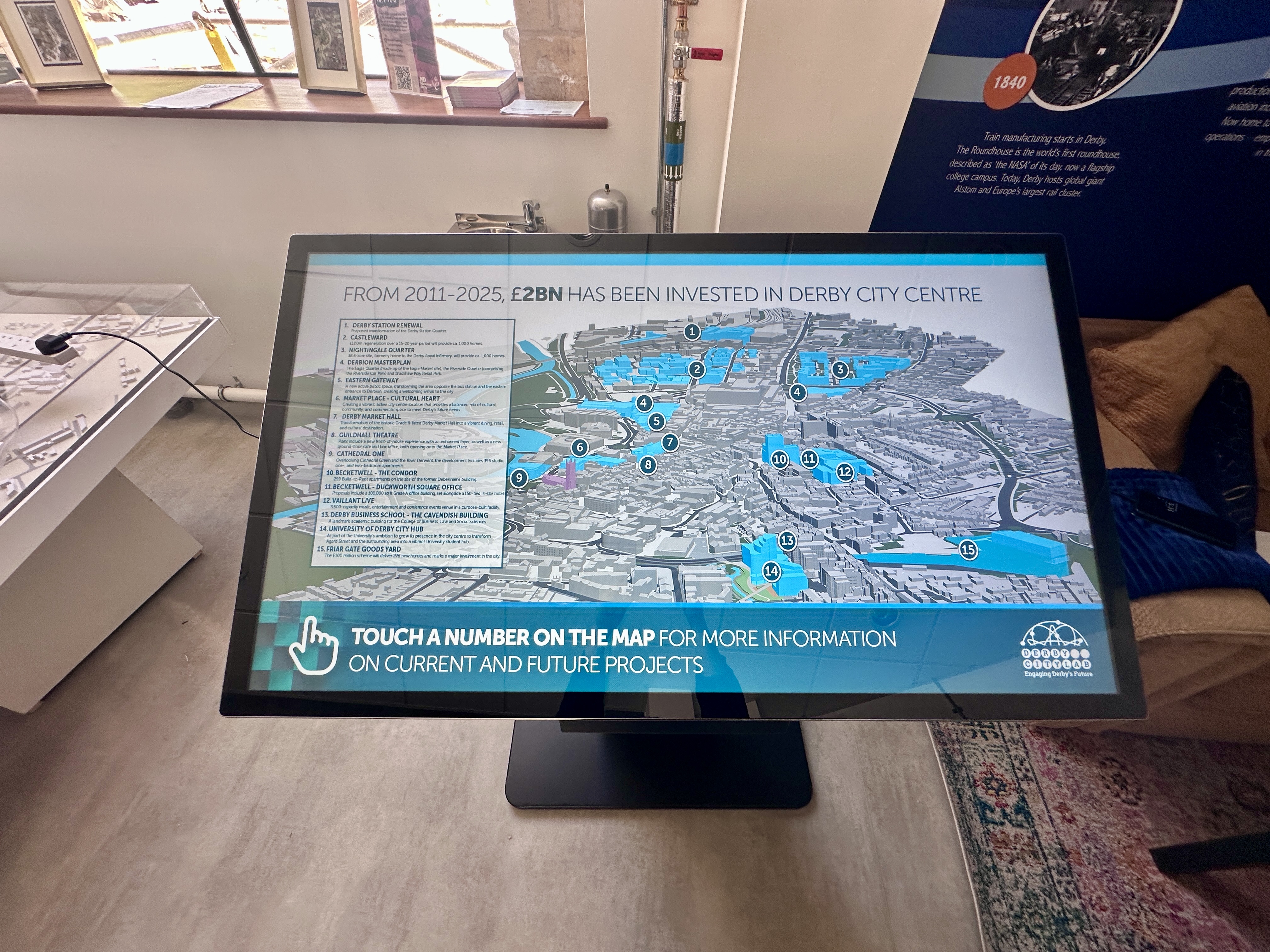 Interactive touchscreen map on a tablet showing Derby city centre with numbered locations and project info