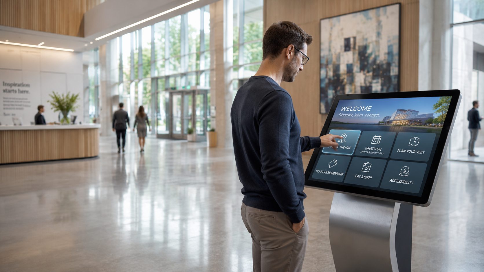 Man in a dark sweater uses a large interactive kiosk in a bright, modern lobby.