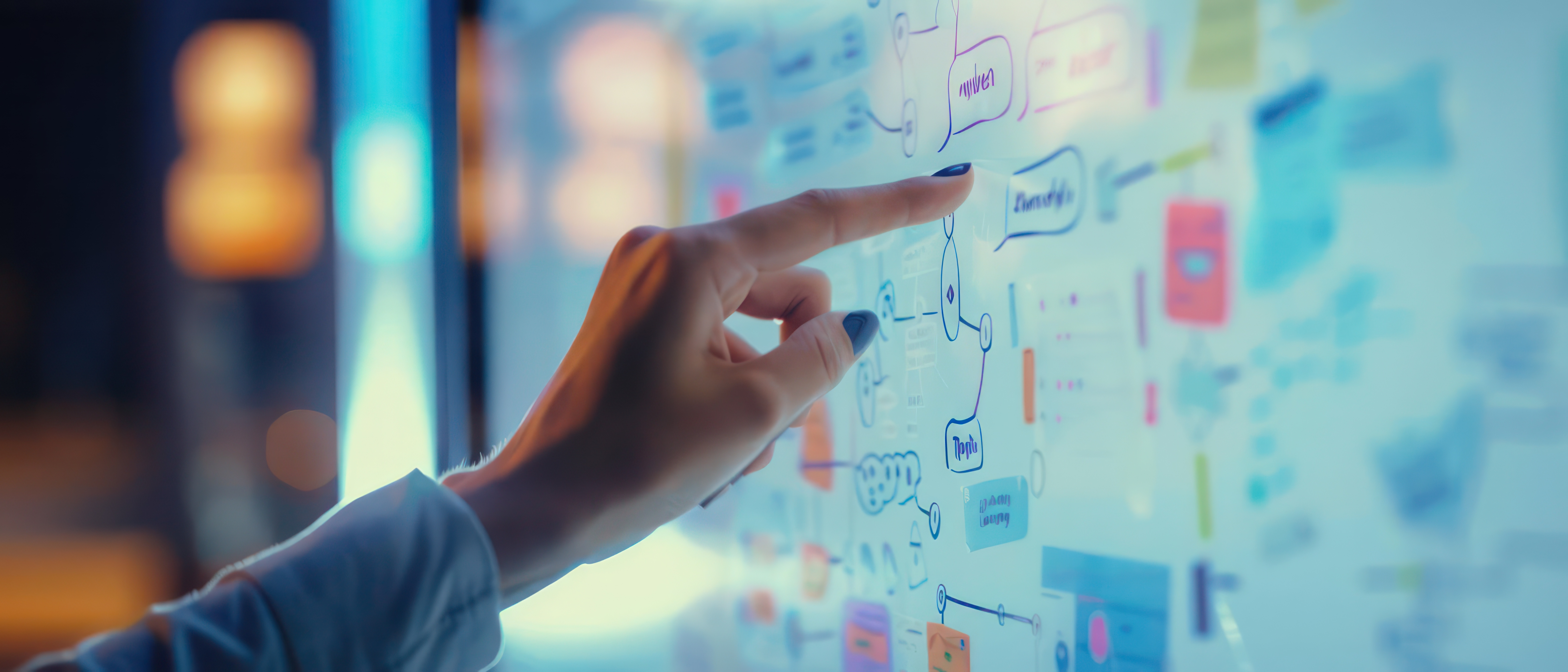 Person’s hand points at a glass wall filled with diagrams and colorful sticky notes during a brainstorming session.
