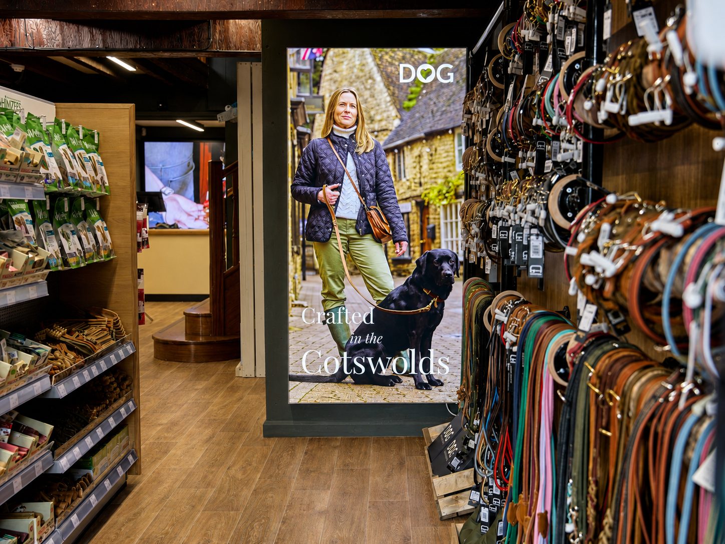Poster in a shop shows a woman with a black dog on a leash in a cobbled street; text reads 'Crafted in the Cotswolds' with a dog-themed brand logo.