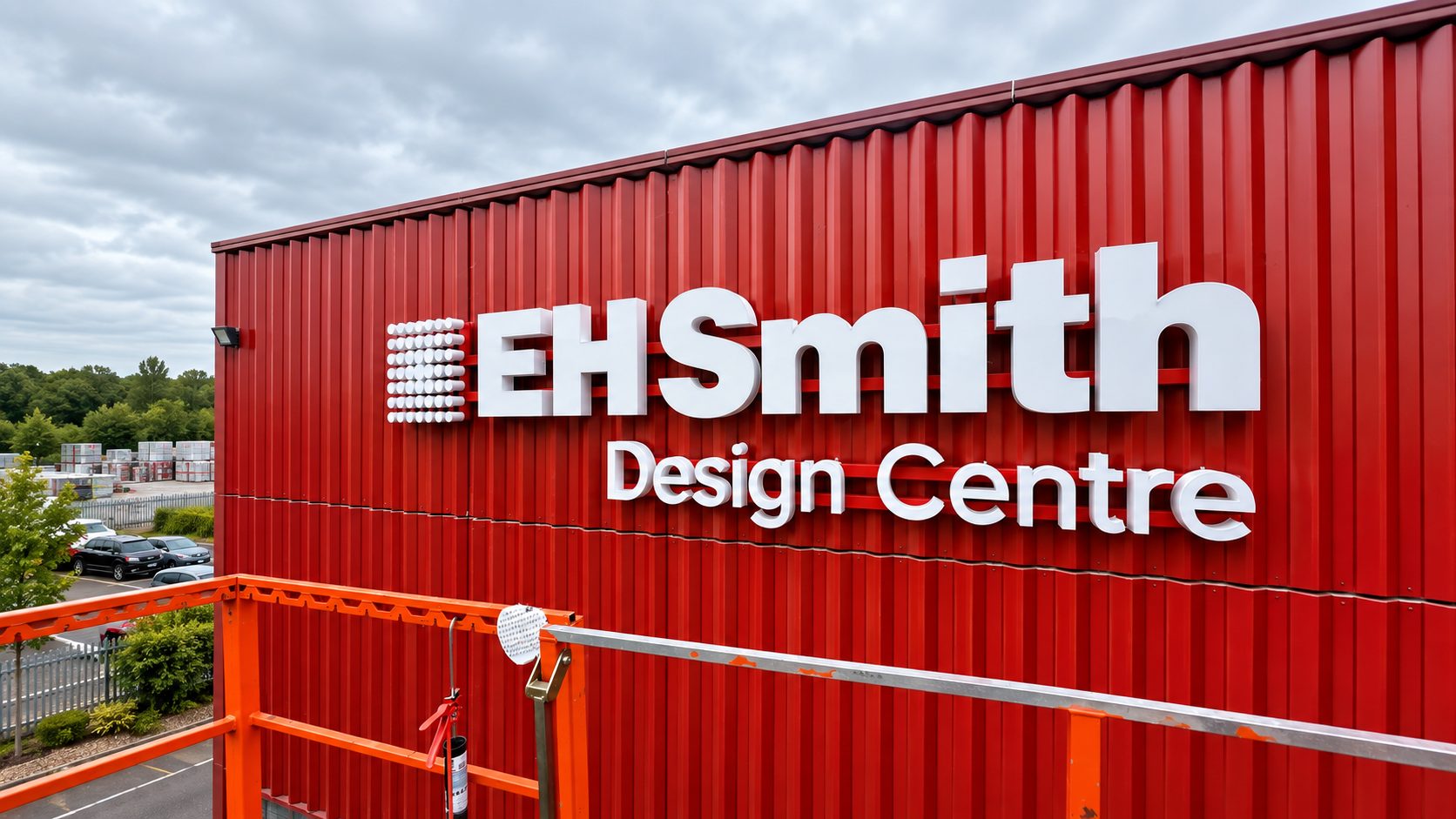 Red corrugated metal building with a large white 'EH Smith Design Centre' sign on the side of the structure, outdoors under a cloudy sky.