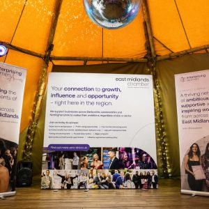 Three banners on a stage inside a yellow tent, promoting women in business; center banner emphasizes growth and opportunity in the region.