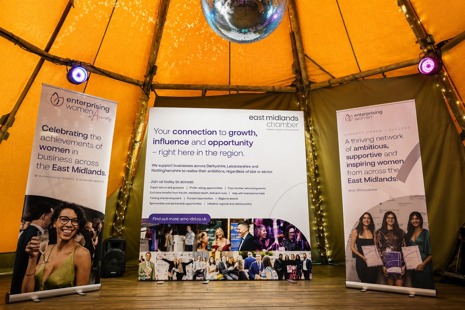 Three banners on a stage inside a yellow tent, promoting women in business; center banner emphasizes growth and opportunity in the region.