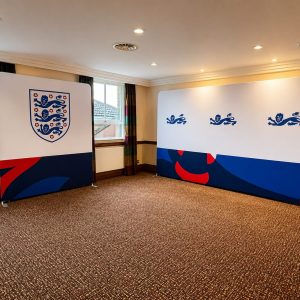 Two large freestanding banners with England flag motifs (three lions crest) set up in a carpeted room, forming a display area for an event.
