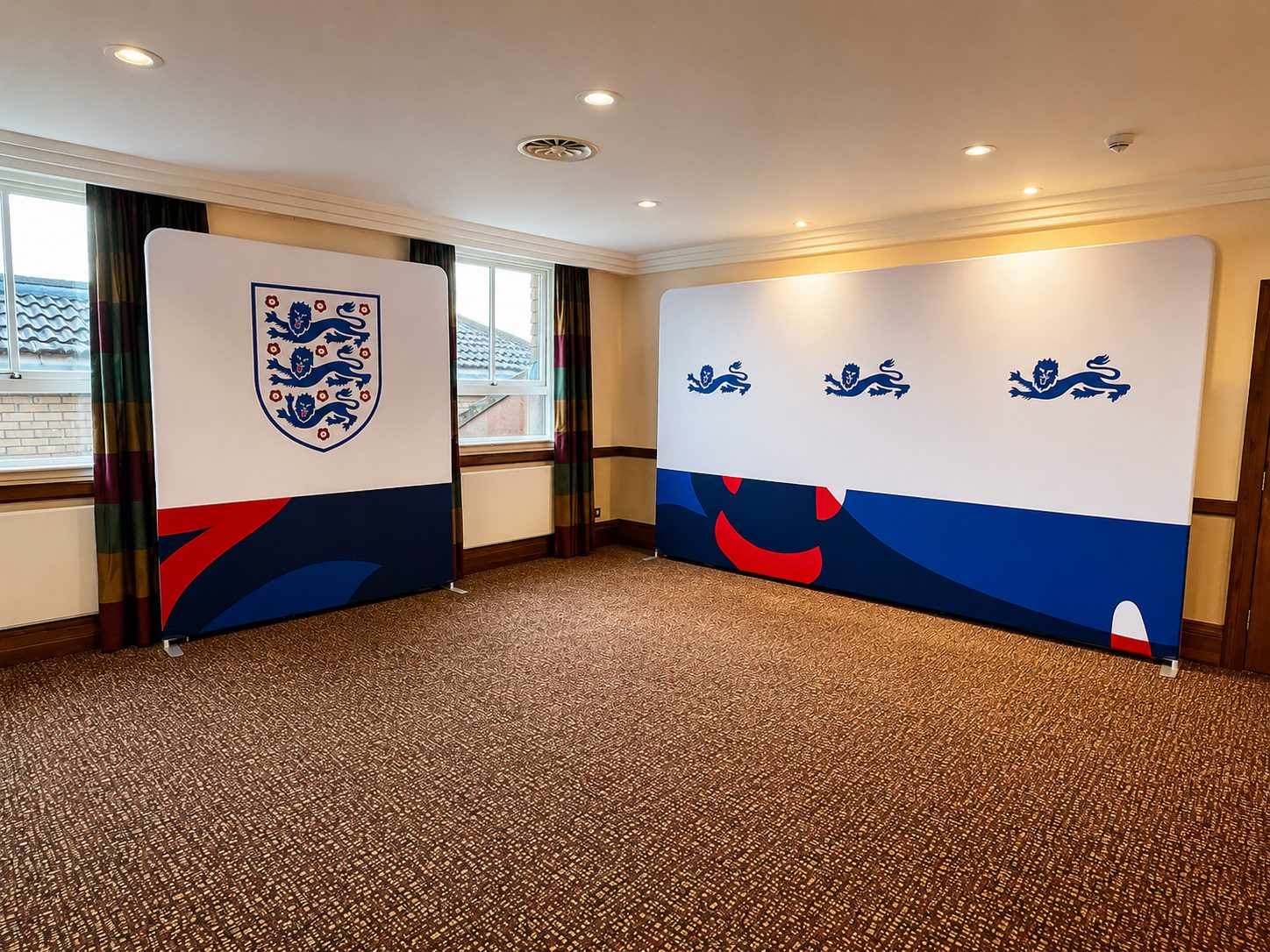 Two large freestanding banners with England flag motifs (three lions crest) set up in a carpeted room, forming a display area for an event.