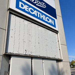 Exterior of a shopping storefront with a large blue-and-white Decathlon sign above a closed shutter decorated with string lights.