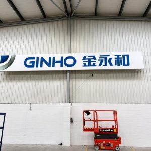 Industrial warehouse interior with a white sign reading GINHO and Chinese characters, and a red scissor lift nearby.