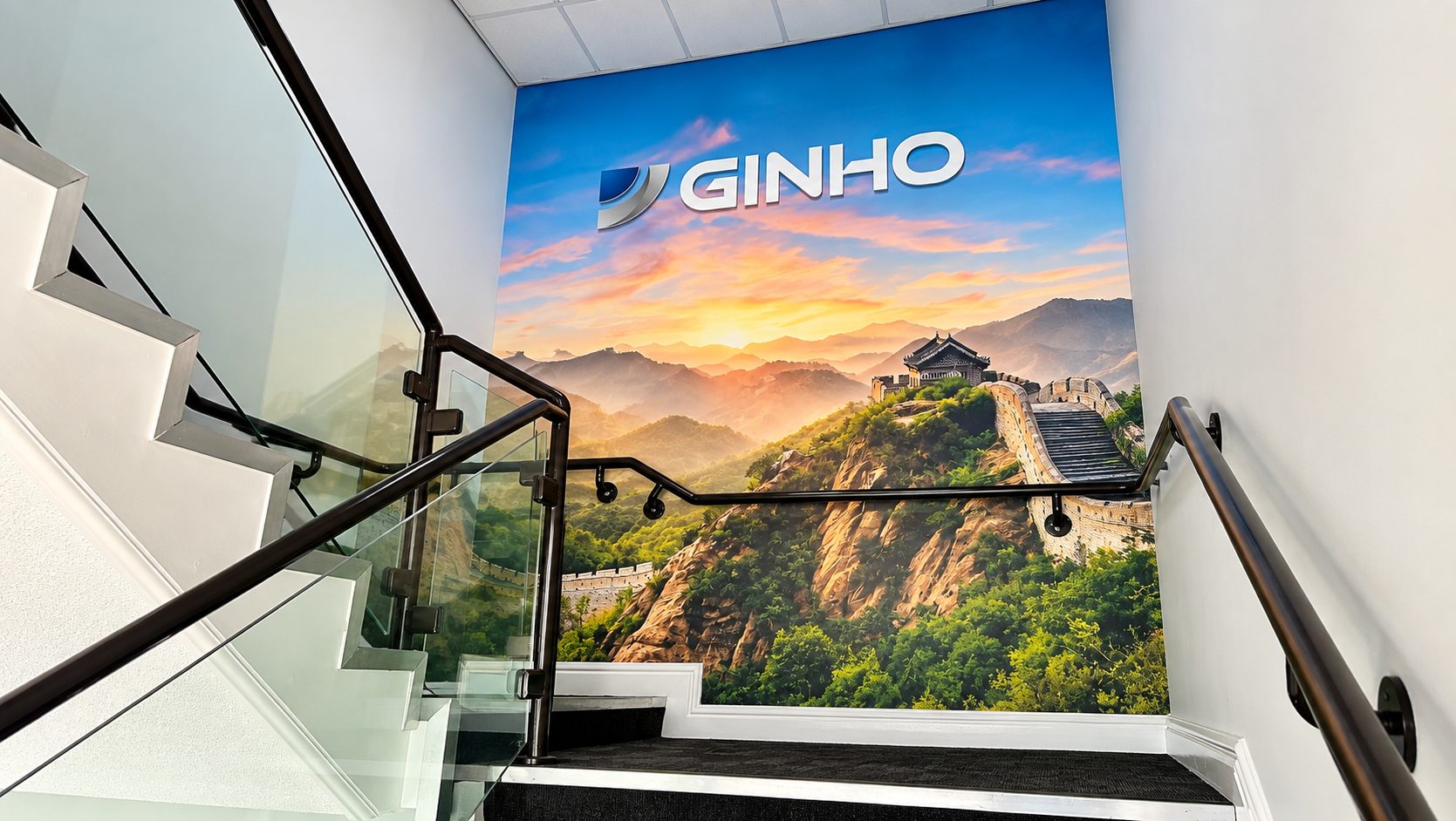Staircase inside a building with a large mural showing mountains, the Great Wall, and the word 'GINHO' at the top.