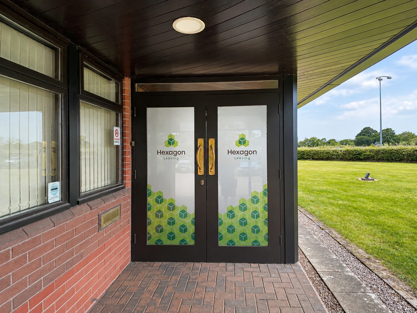 Double glass doors with Hexagon Leasing logo and a green hexagon pattern at the bottom, at an office entrance behind a brick wall.