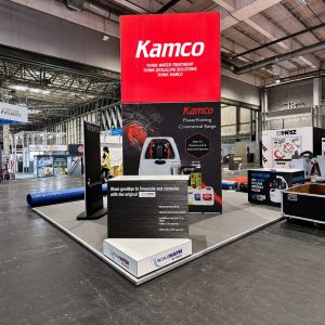 Industrial exhibition booth with a tall red Kamco sign and dark display panels showcasing water treatment equipment in a large convention hall