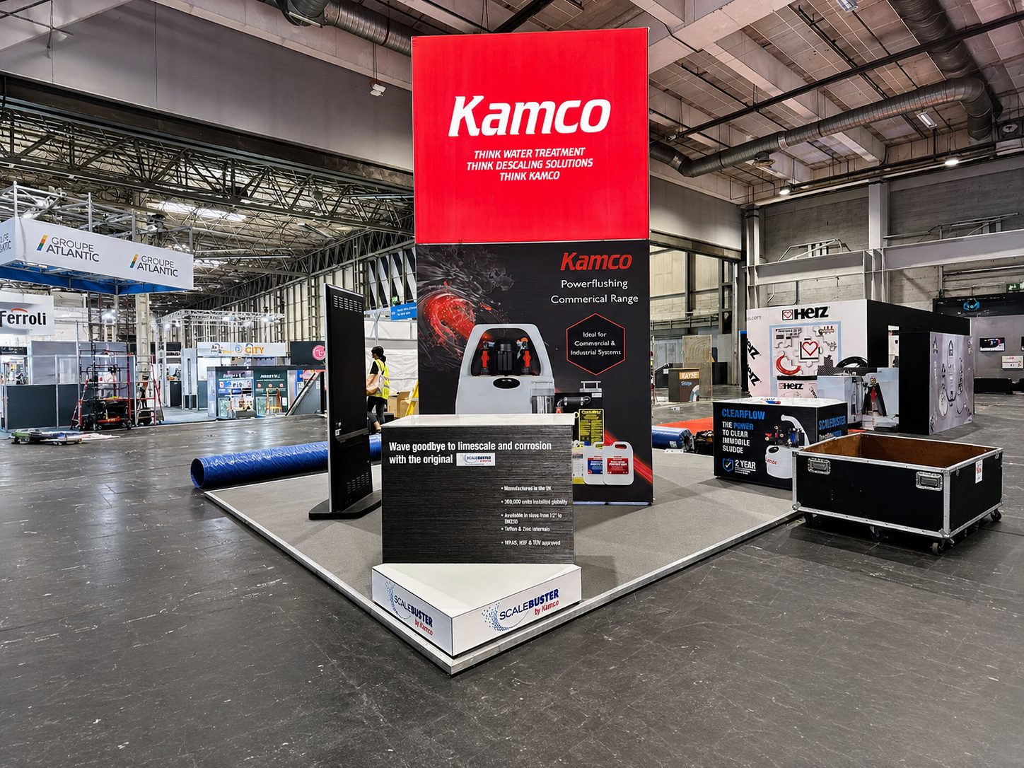Industrial exhibition booth with a tall red Kamco sign and dark display panels showcasing water treatment equipment in a large convention hall
