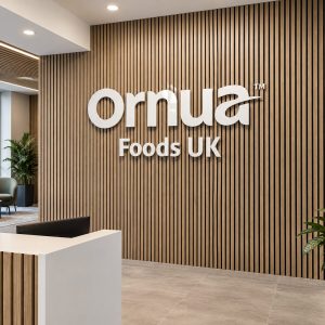 Reception area with vertical wood slat wall and large white 'Ornua Foods UK' sign on the wall behind a white reception desk with a black chair nearby.- informational, concise (125 chars)
