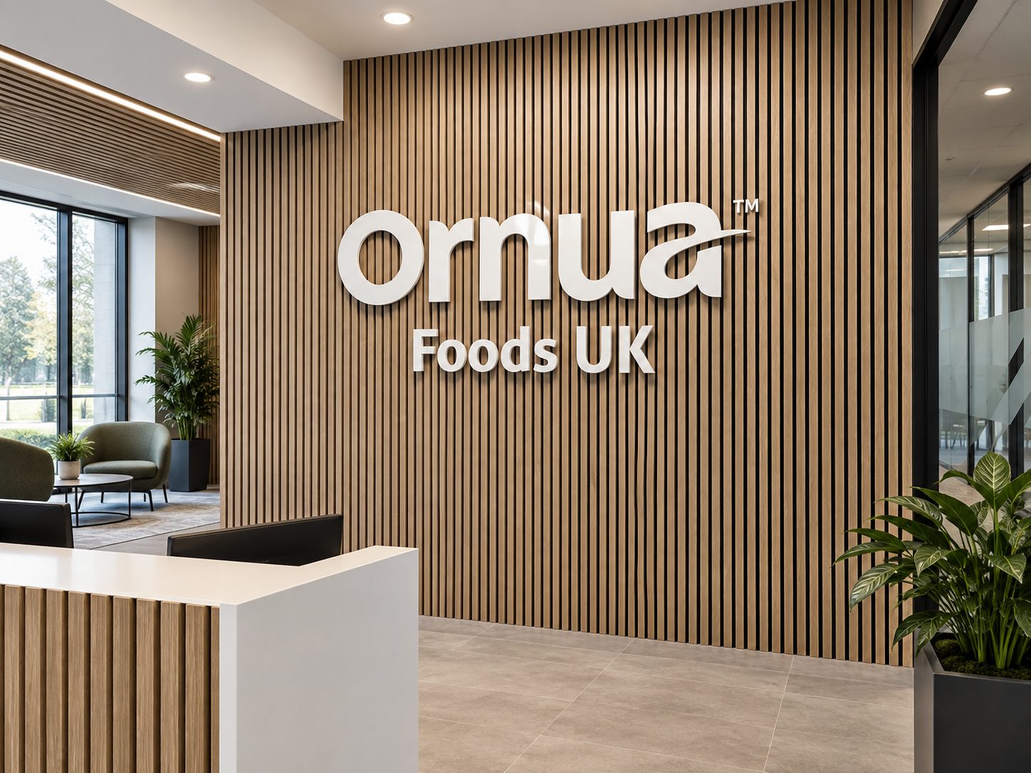 Reception area with vertical wood slat wall and large white 'Ornua Foods UK' sign on the wall behind a white reception desk with a black chair nearby.- informational, concise (125 chars)