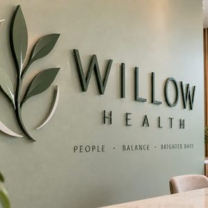 Reception area with a green wall showing the Willow Health logo and the motto 'People · Balance · Brighter Days'.