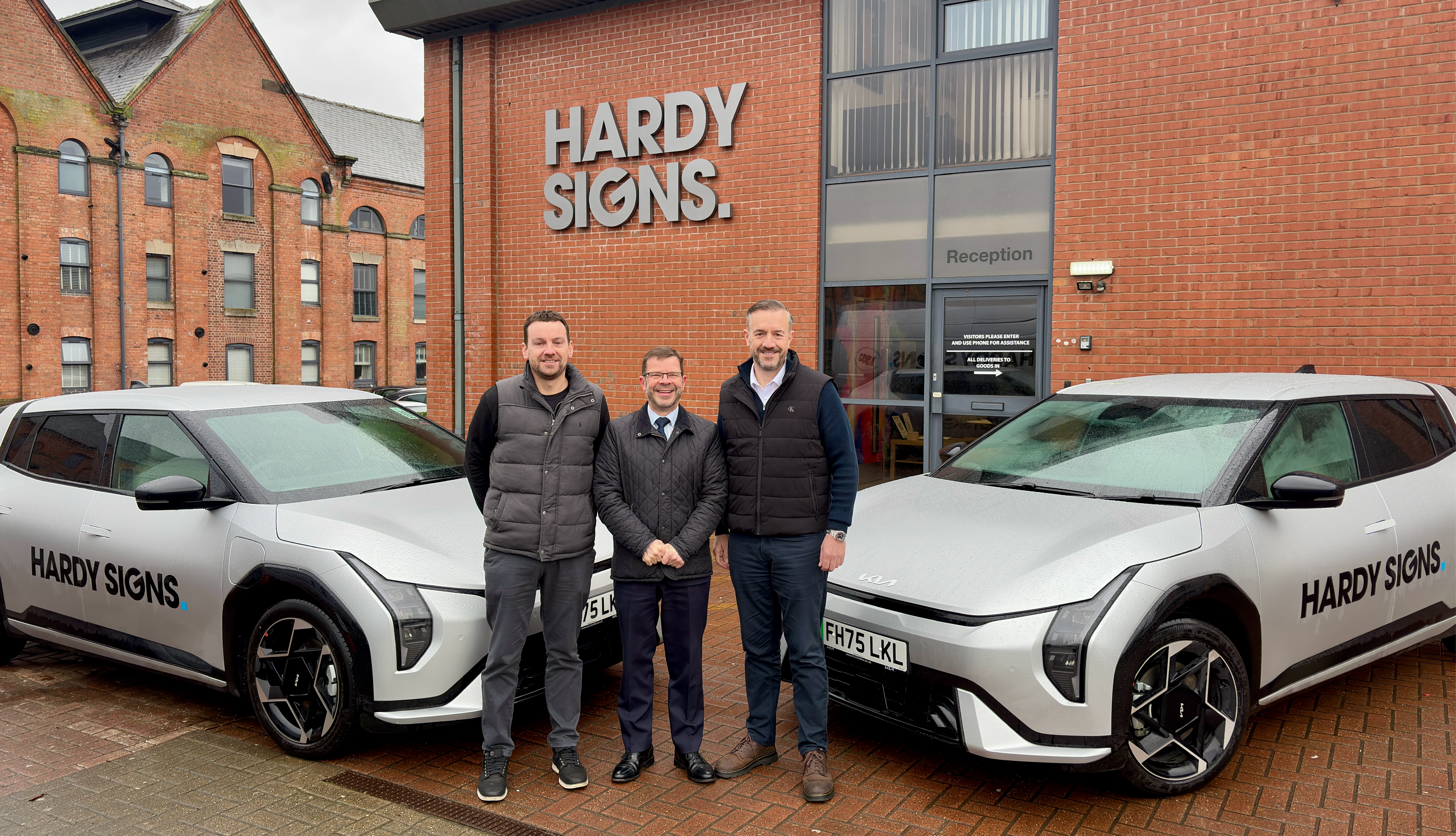 Tom Hardy Nik Hardy and Dale Bywater standing next to two new EV cars from Burton KIA