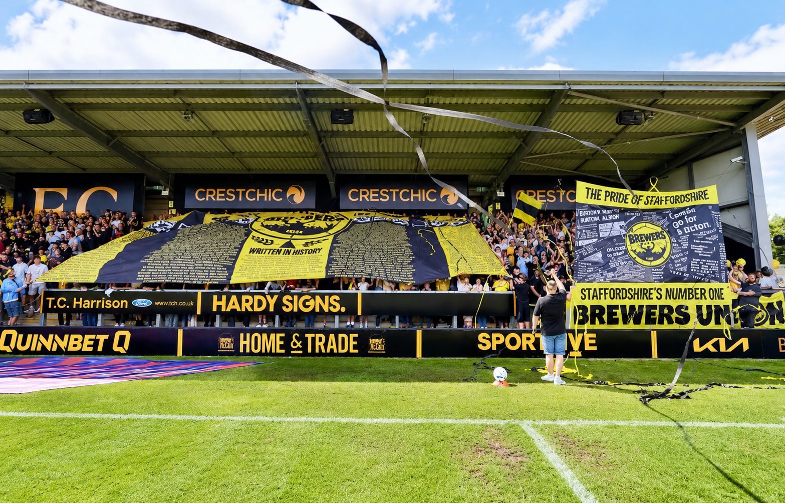 Crowd of football fans in yellow and black, cheering from stadium stands with large banners and streamers