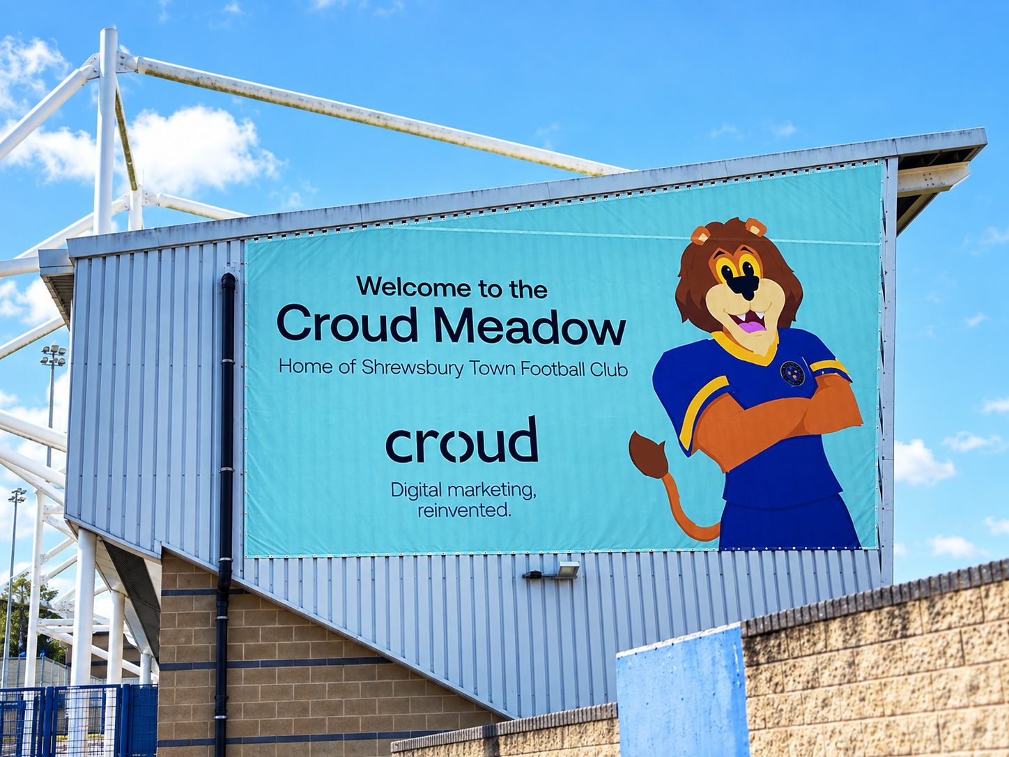 Large turquoise stadium banner reading 'Welcome to the Croud Meadow' with a cartoon lion mascot in blue and yellow armor.