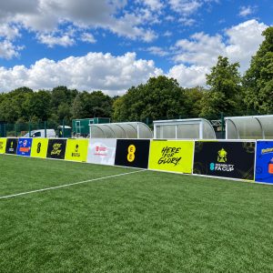 Row of colorful advertising banners along a football pitch beside the team benches on a sunny day.