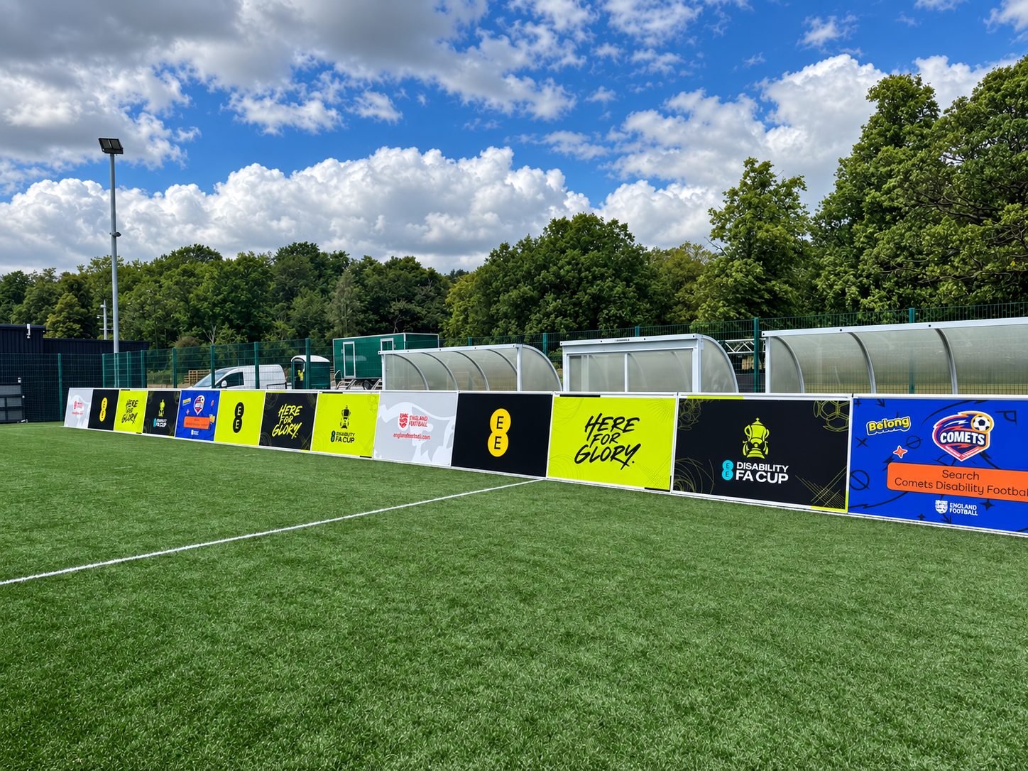 Row of colorful advertising banners along a football pitch beside the team benches on a sunny day.