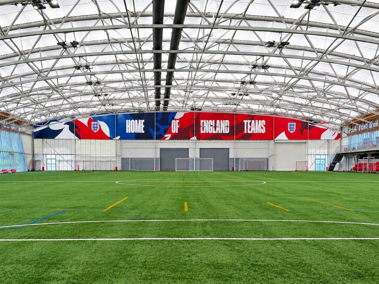 Indoor artificial turf soccer field with a large banner reading 'HOME OF ENGLAND TEAMS' along the back wall.