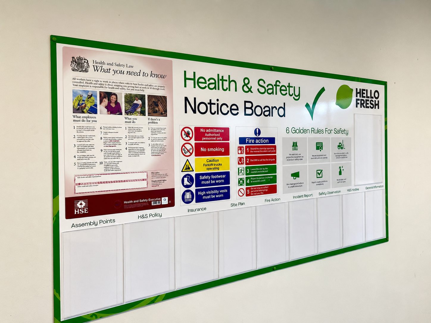 Health & Safety Notice Board mounted on a wall with charts, lists and a Hello Fresh logo on the right side.