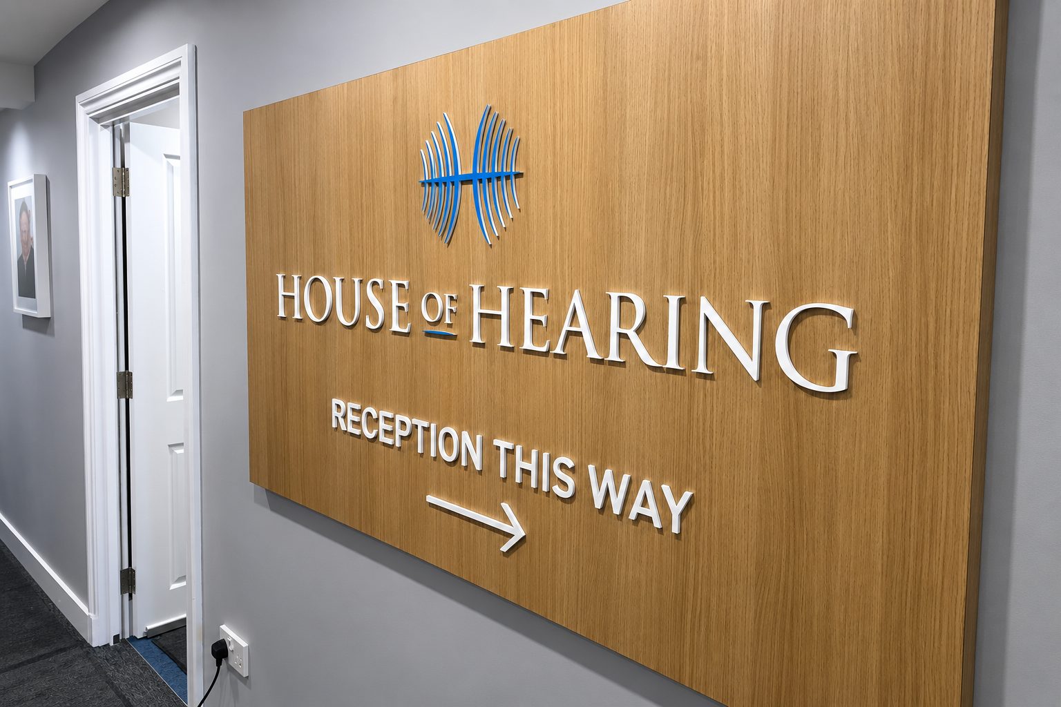 Wood-paneled sign reading 'HOUSE OF HEARING' with a blue logo and 'RECEPTION THIS WAY' arrow.