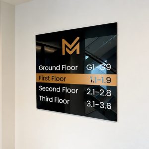 Interior directory sign on a wall listing floor ranges: Ground Floor G1–G9, First Floor 1.1–1.9, Second Floor 2.1–2.8, Third Floor 3.1–3.6, with an orange M logo.
