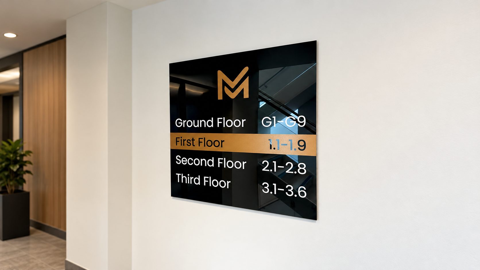 Interior directory sign on a wall listing floor ranges: Ground Floor G1–G9, First Floor 1.1–1.9, Second Floor 2.1–2.8, Third Floor 3.1–3.6, with an orange M logo.